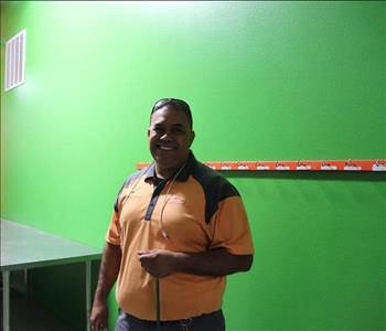 Man in orange shirt standing in front of green painted wall.