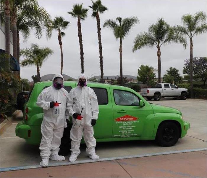 Two employees dressed in PPE in front of SERVPRO car 
