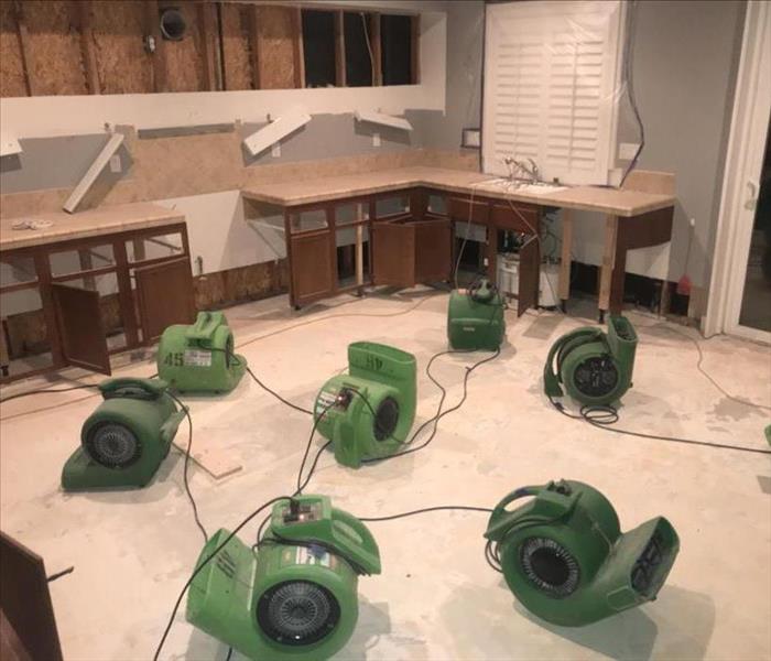 Green air movers and dehumidifiers in large room.